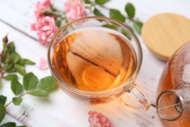 Photo of Tasty rose tea in glass cup, flowers and leaves on white wooden table, closeup