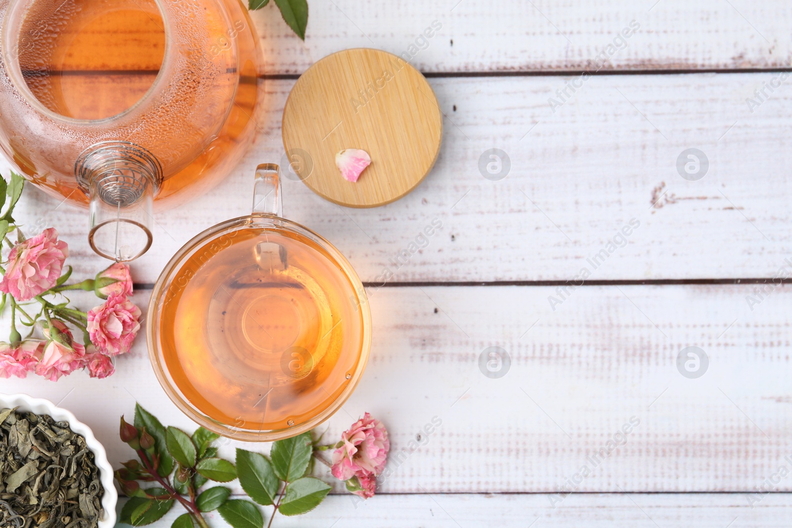 Tasty rose tea in glass cup, teapot, flowers and leaves on light wooden table, flat lay. Space for text Photo of Tasty rose tea in glass cup, teapot, flowers and leaves on light wooden table, flat lay. Space for text