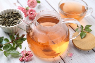 Photo of Tasty rose tea, flowers and leaves on white wooden table, closeup