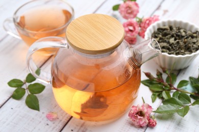 Photo of Tasty rose tea, flowers and leaves on white wooden table, closeup