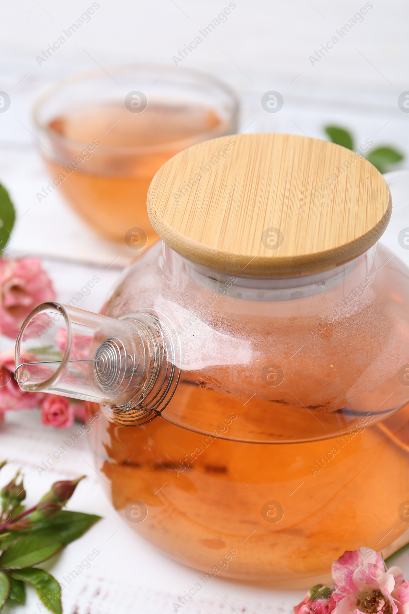 Tasty rose tea in glass teapot, flowers and leaves on white wooden table, closeup Photo of Tasty rose tea in glass teapot, flowers and leaves on white wooden table, closeup