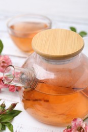 Photo of Tasty rose tea in glass teapot, flowers and leaves on white wooden table, closeup