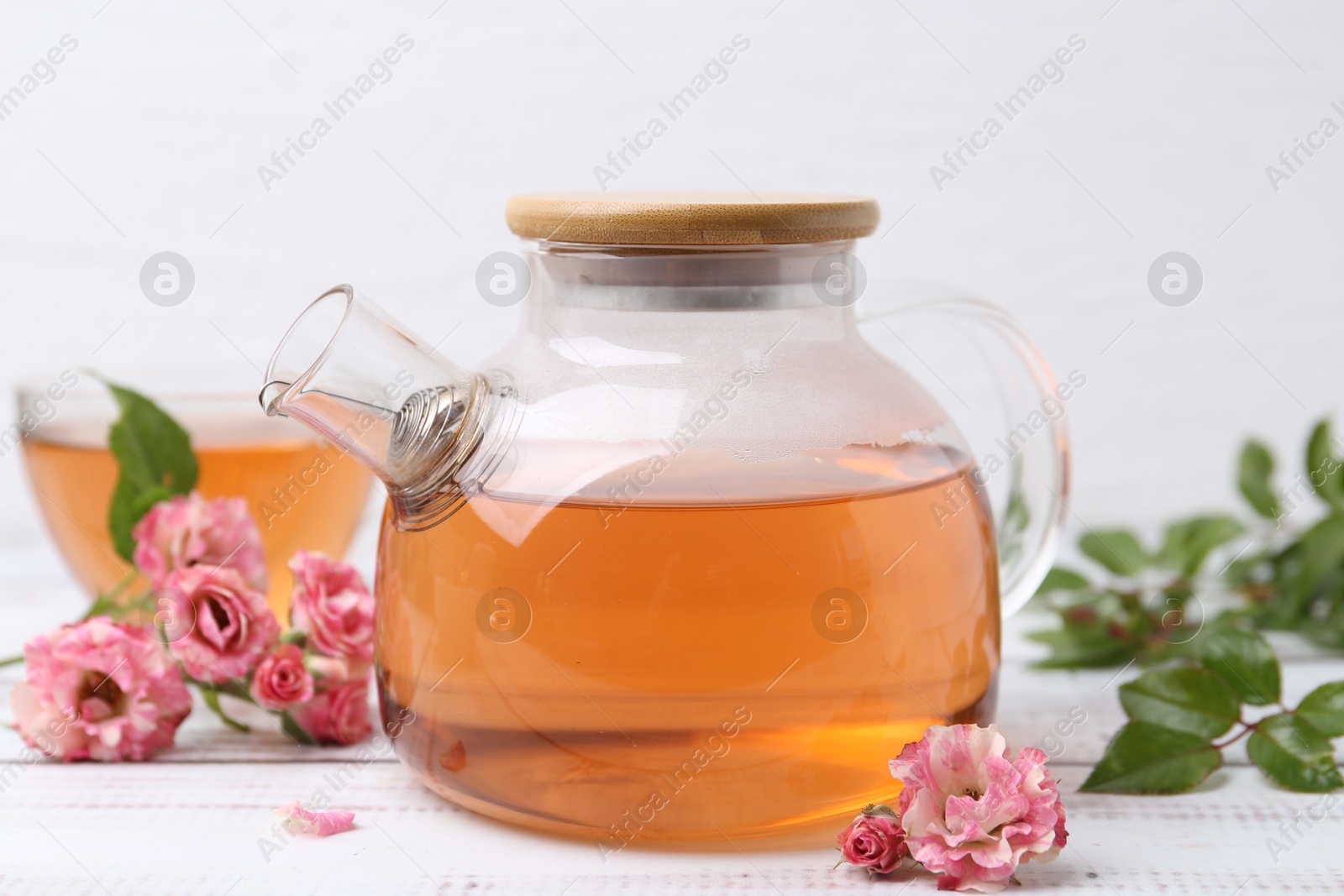 Tasty rose tea in glass teapot, flowers and leaves on white wooden table, closeup Photo of Tasty rose tea in glass teapot, flowers and leaves on white wooden table, closeup