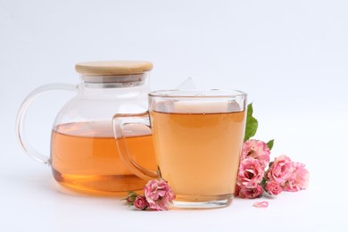 Photo of Tasty rose tea in glass cup, teapot and flowers on white background