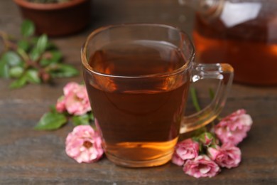 Photo of Tasty rose tea in glass cup and flowers on wooden table, closeup