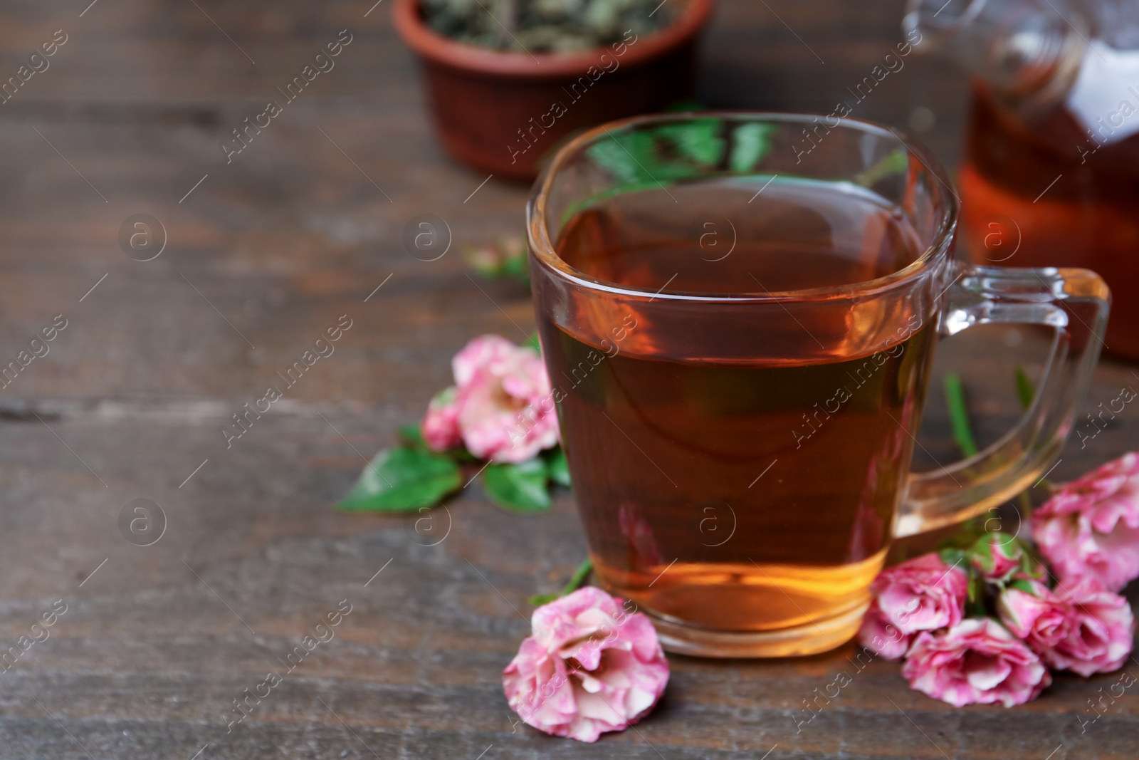 Tasty rose tea in glass cup and flowers on wooden table, closeup Photo of Tasty rose tea in glass cup and flowers on wooden table, closeup