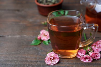 Photo of Tasty rose tea in glass cup and flowers on wooden table, closeup