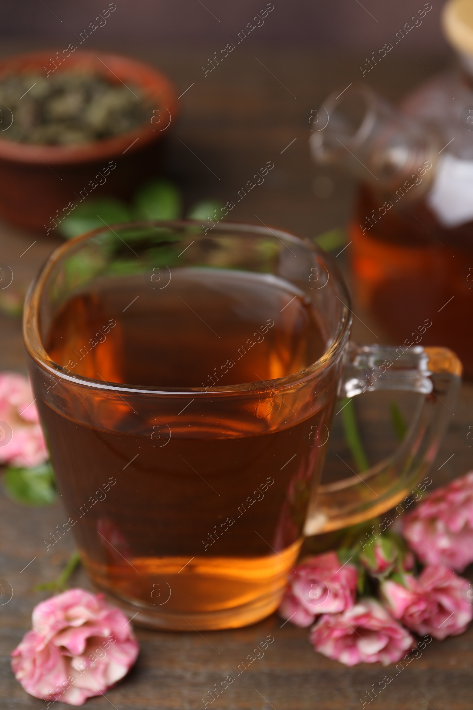 Photo of Tasty rose tea in glass cup and flowers on wooden table, closeup