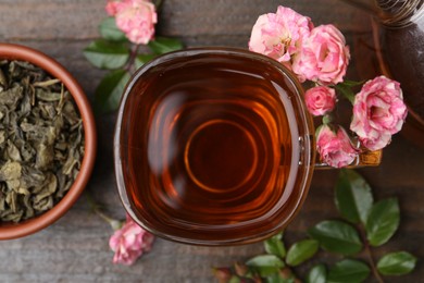 Photo of Tasty rose tea in glass cup, flowers and leaves on wooden table, flat lay