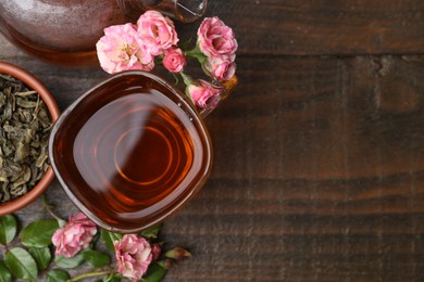 Photo of Tasty rose tea in glass cup, flowers and leaves on wooden table, flat lay. Space for text