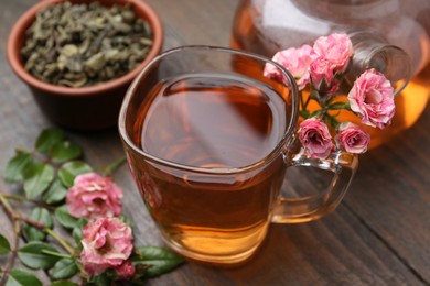 Photo of Tasty rose tea in glass cup, flowers and leaves on wooden table, closeup