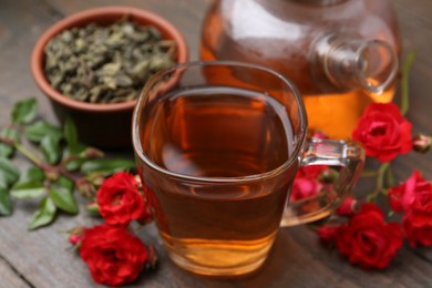 Photo of Tasty rose tea in glass cup, flowers and leaves on wooden table, closeup
