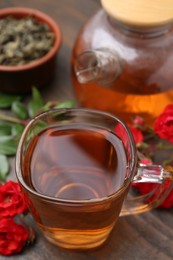 Photo of Tasty rose tea in glass cup, flowers and leaves on wooden table, closeup