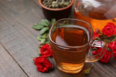Photo of Tasty rose tea in glass cup, flowers and leaves on wooden table, closeup