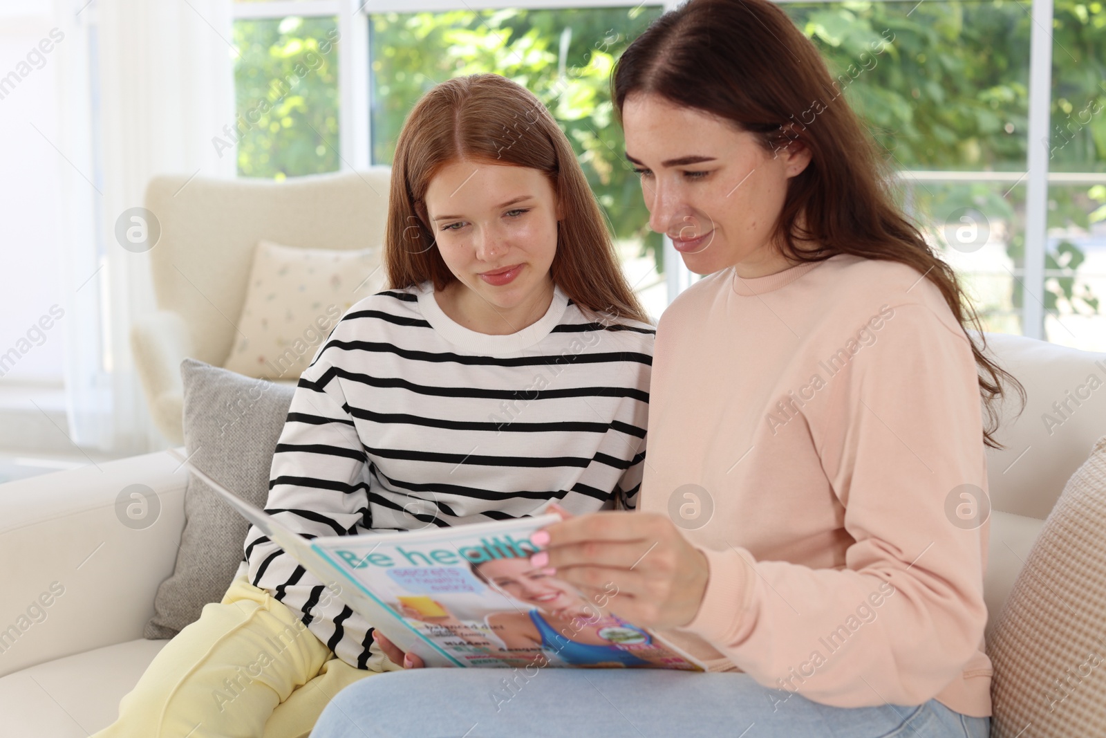 Photo of Mother and her teenage daughter reading magazine together at home