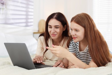 Photo of Mother and her teenage daughter with laptop spending time together on bed at home