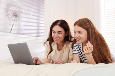 Photo of Mother and her teenage daughter with laptop spending time together on bed at home