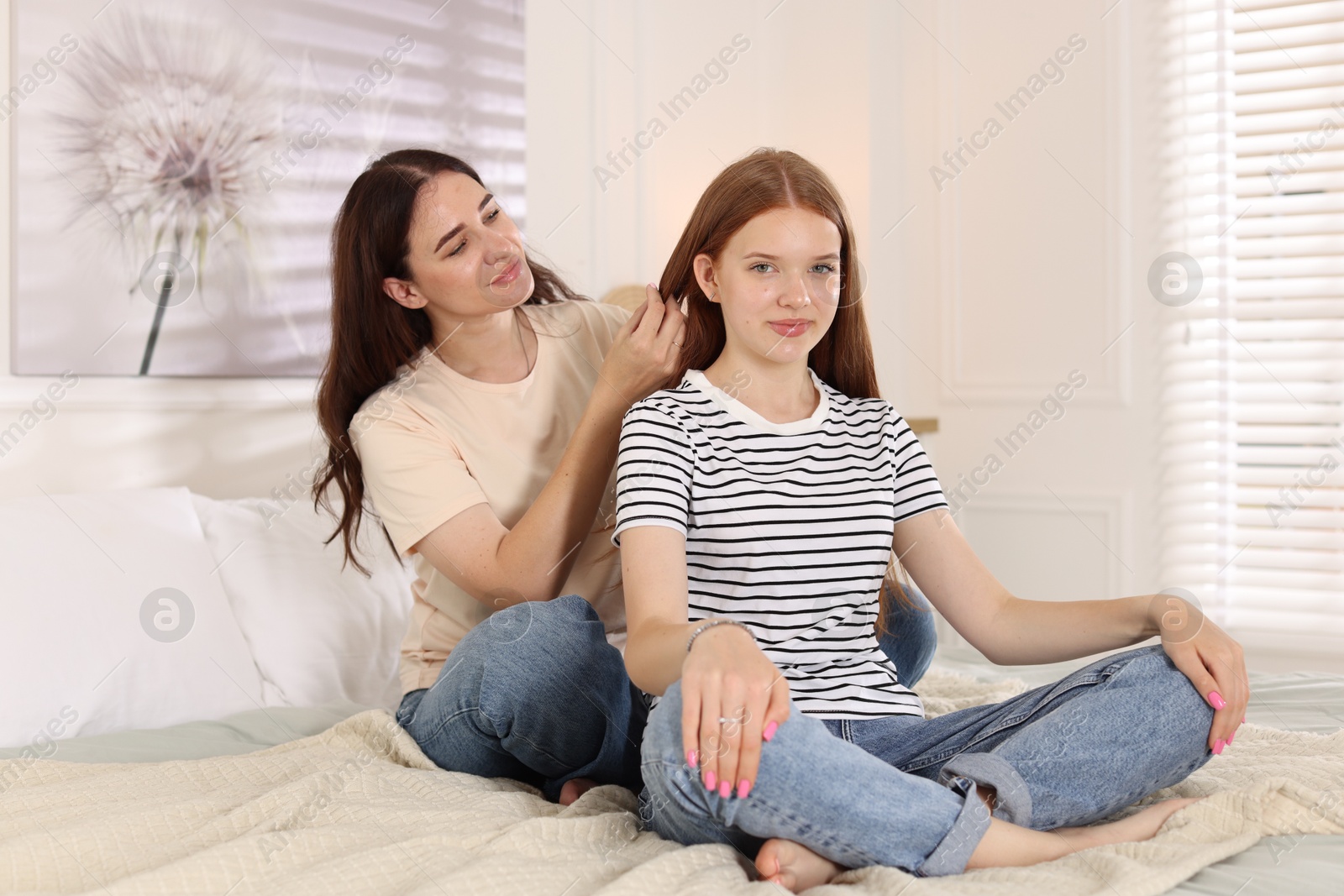 Mother braiding her teenage daughter's hair on bed at home Photo of Mother braiding her teenage daughter's hair on bed at home