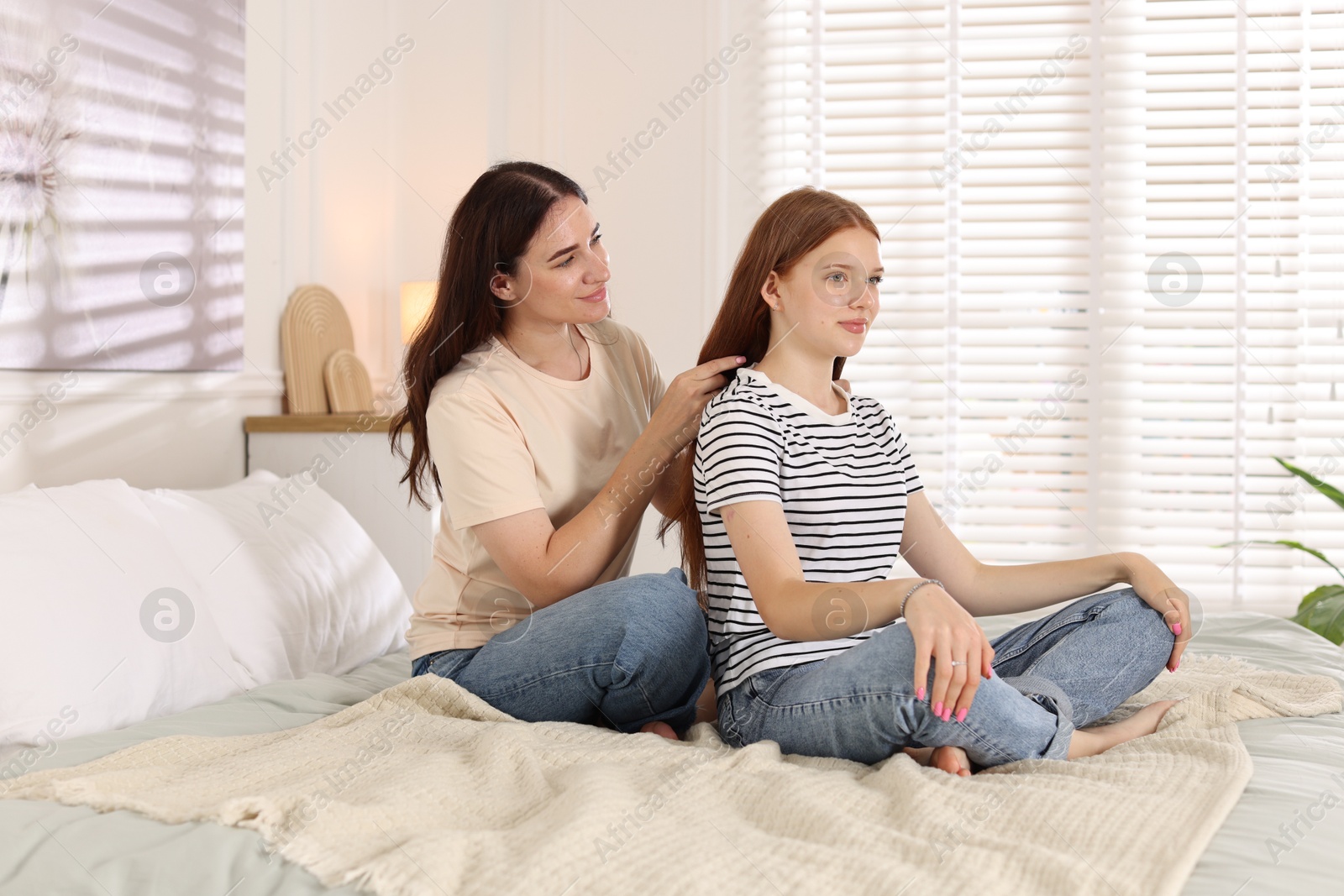 Mother braiding her teenage daughter's hair on bed at home Photo of Mother braiding her teenage daughter's hair on bed at home