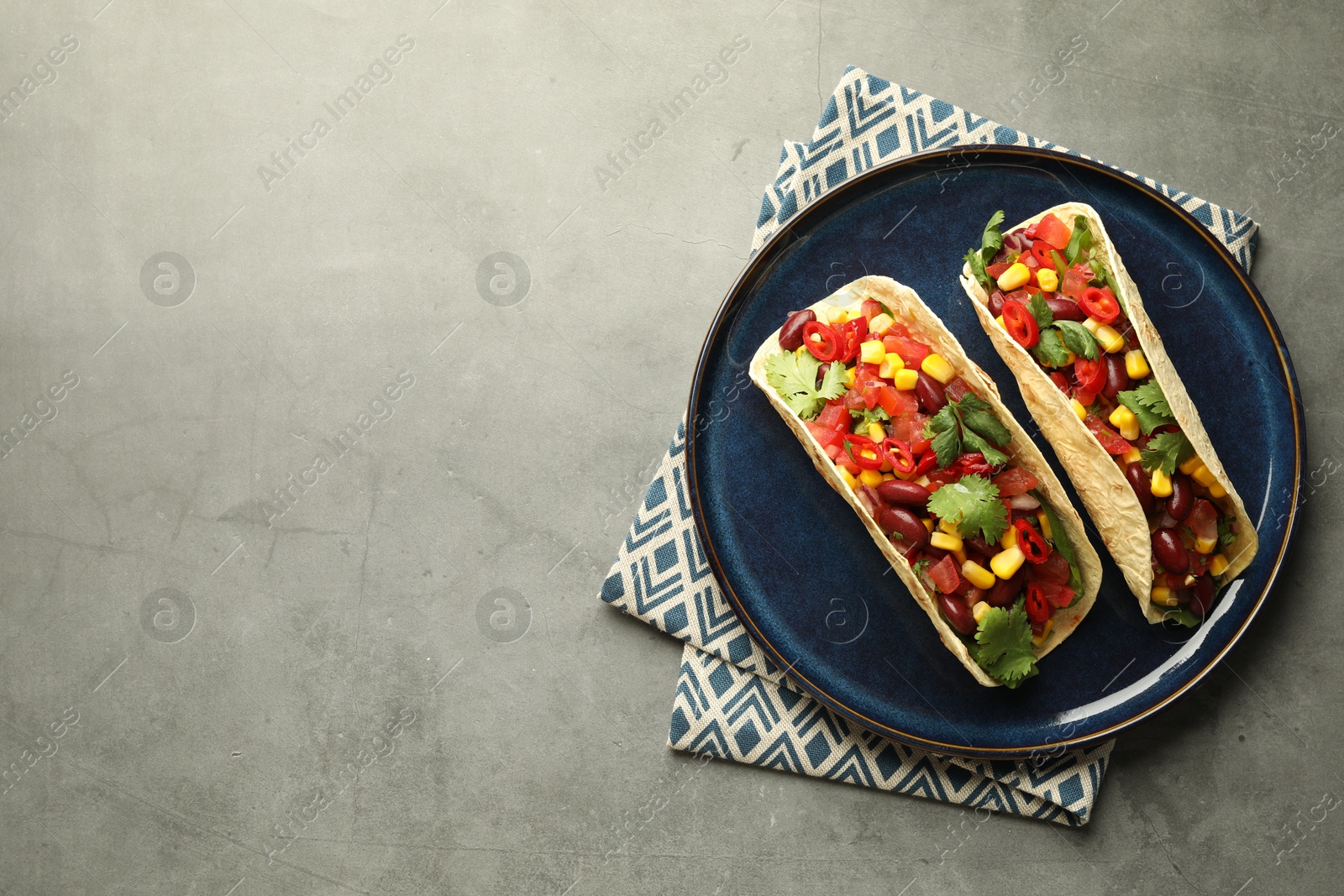 Photo of Tasty vegetarian tacos with beans and vegetables on grey table, top view. Space for text