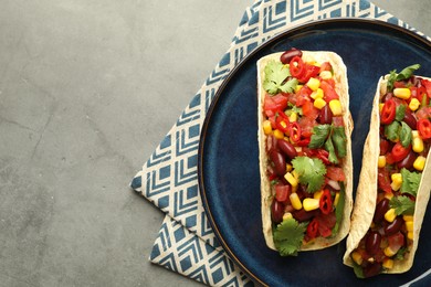 Photo of Tasty vegetarian tacos with beans and vegetables on grey table, top view. Space for text