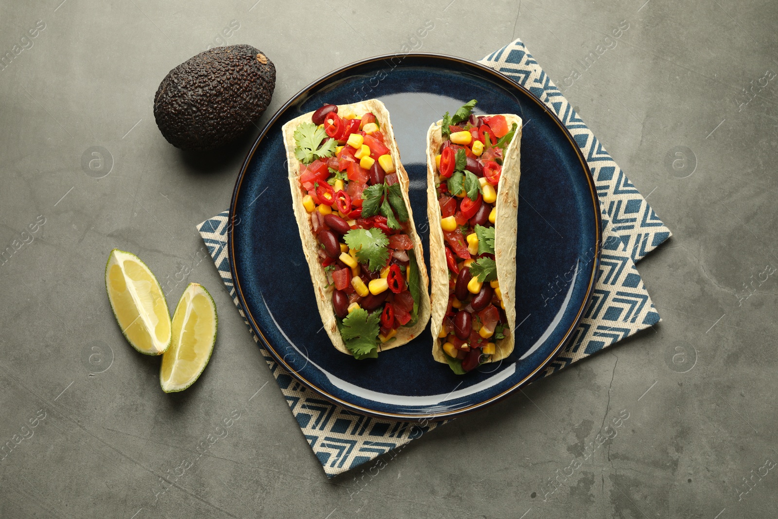 Photo of Tasty vegetarian tacos with beans, vegetables, avocado and lime on grey table, flat lay