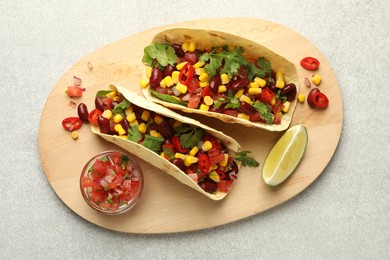 Photo of Tasty vegetarian tacos with beans, vegetables and lime on light grey table, top view