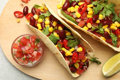 Photo of Tasty vegetarian tacos with beans, vegetables and lime on light grey table, top view