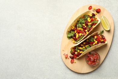 Photo of Tasty vegetarian tacos with beans, vegetables and lime on light grey table, top view. Space for text