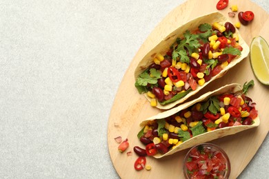 Photo of Tasty vegetarian tacos with beans, vegetables and lime on light grey table, top view. Space for text