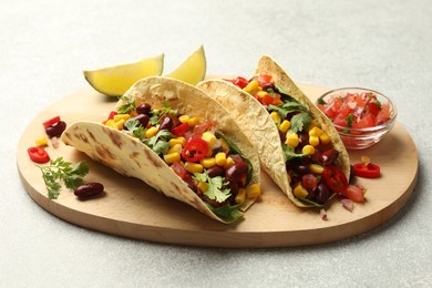 Photo of Tasty vegetarian tacos with beans, vegetables and lime on light grey table, closeup