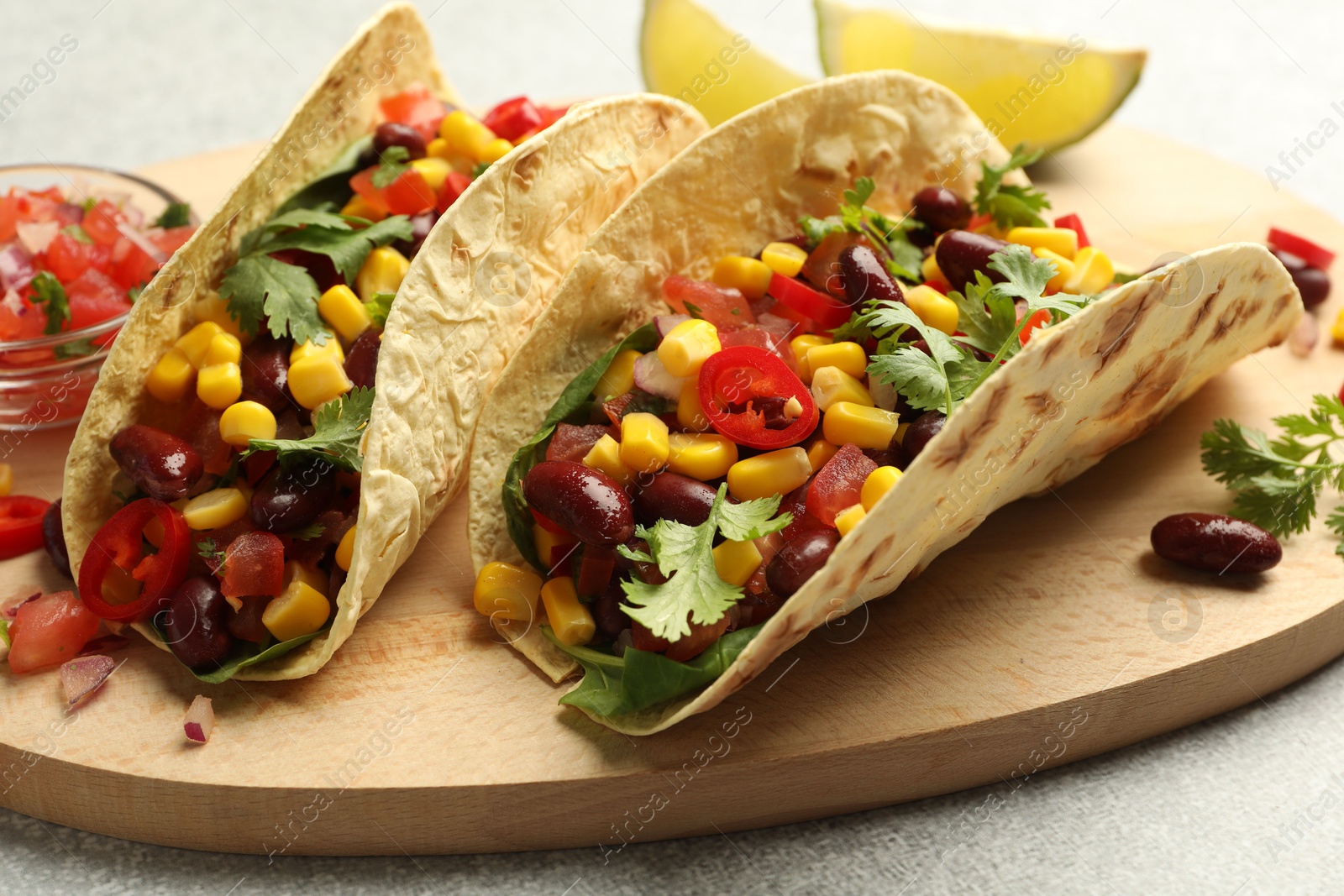 Photo of Tasty vegetarian tacos with beans, vegetables and lime on light grey table, closeup