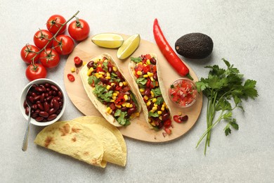 Photo of Tasty vegetarian tacos and ingredients on light grey table, flat lay