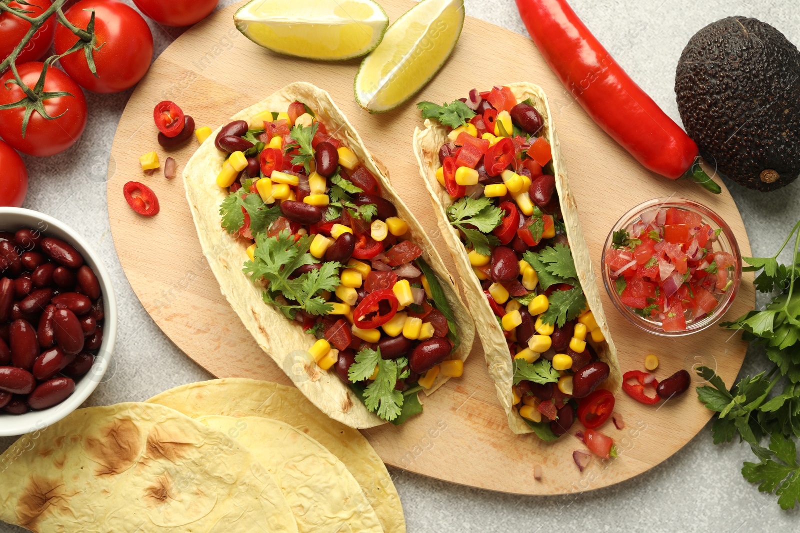 Photo of Tasty vegetarian tacos and ingredients on light grey table, flat lay