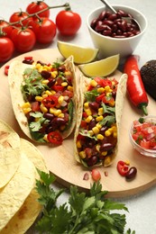Photo of Tasty vegetarian tacos and ingredients on light grey table, closeup