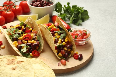 Photo of Tasty vegetarian tacos and ingredients on light grey table, closeup