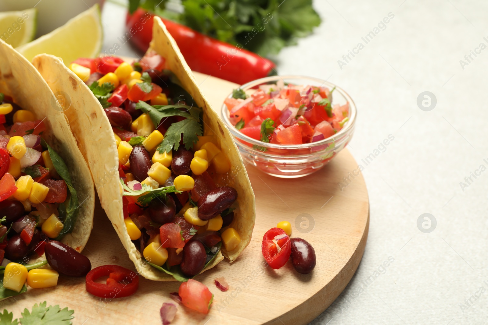 Photo of Tasty vegetarian tacos and ingredients on light grey table, closeup