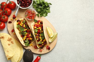 Photo of Tasty vegetarian tacos and ingredients on light grey table, flat lay. Space for text