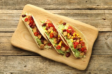 Photo of Tasty vegetarian tacos with beans, tofu and vegetables on wooden table, top view