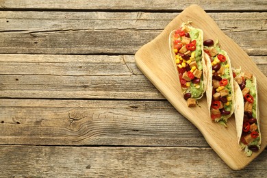 Photo of Tasty vegetarian tacos with beans, tofu and vegetables on wooden table, top view. Space for text