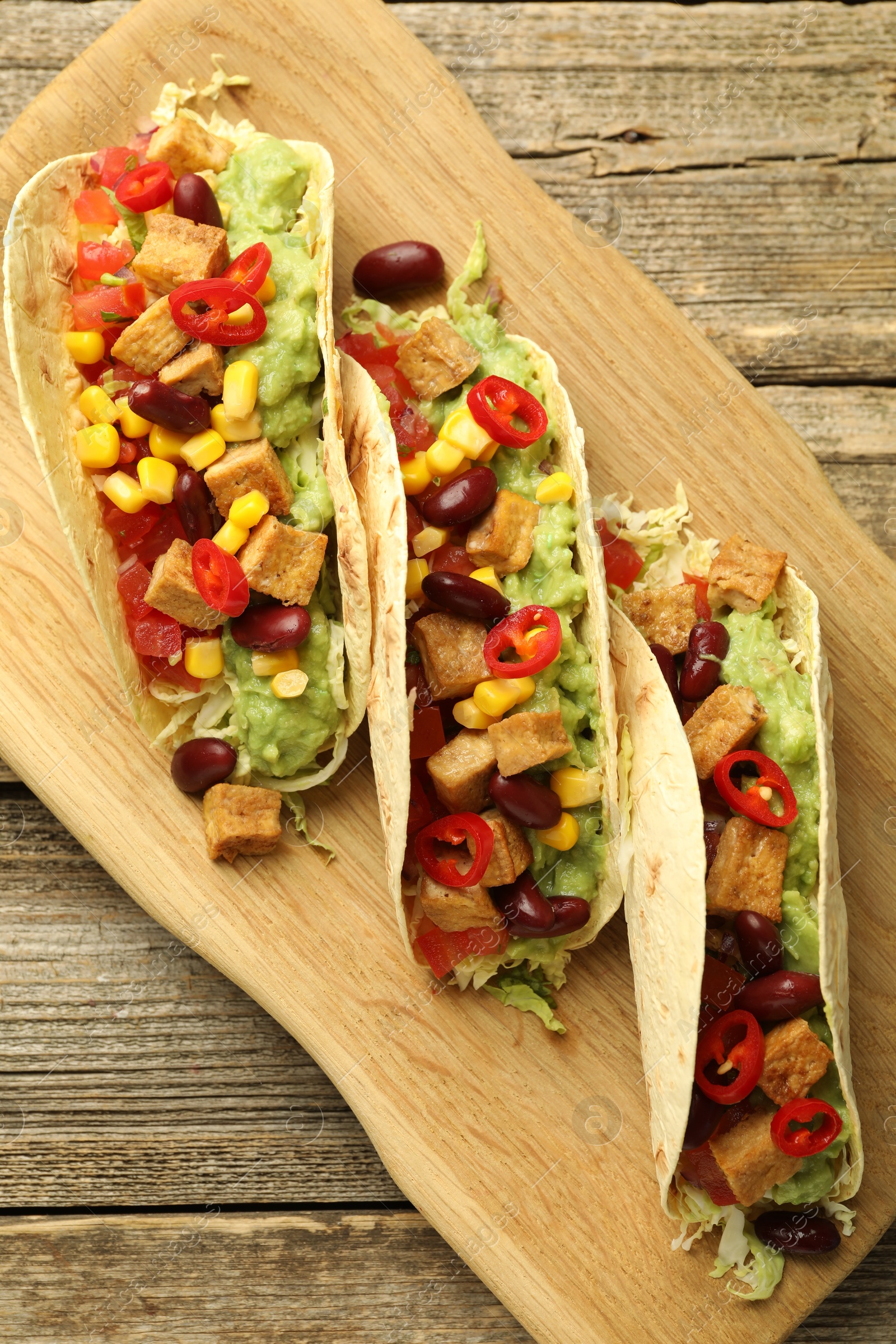 Photo of Tasty vegetarian tacos with beans, tofu and vegetables on wooden table, top view