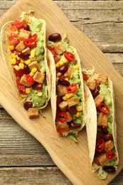 Photo of Tasty vegetarian tacos with beans, tofu and vegetables on wooden table, top view