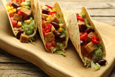 Photo of Tasty vegetarian tacos with beans, tofu and vegetables on wooden table, closeup