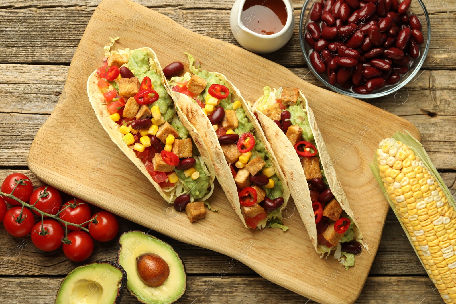 Photo of Tasty vegetarian tacos and ingredients on wooden table, flat lay