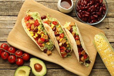 Photo of Tasty vegetarian tacos and ingredients on wooden table, flat lay