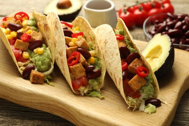 Photo of Tasty vegetarian tacos and ingredients on wooden table, closeup