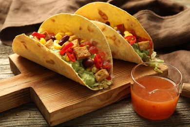 Photo of Tasty vegetarian tacos served with sauce on wooden table, closeup