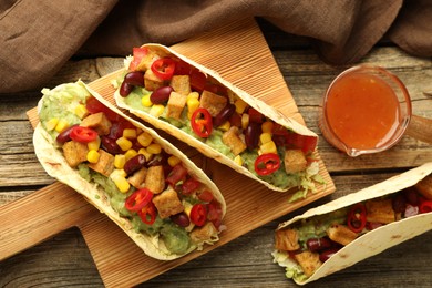 Photo of Tasty vegetarian tacos served with sauce on wooden table, flat lay