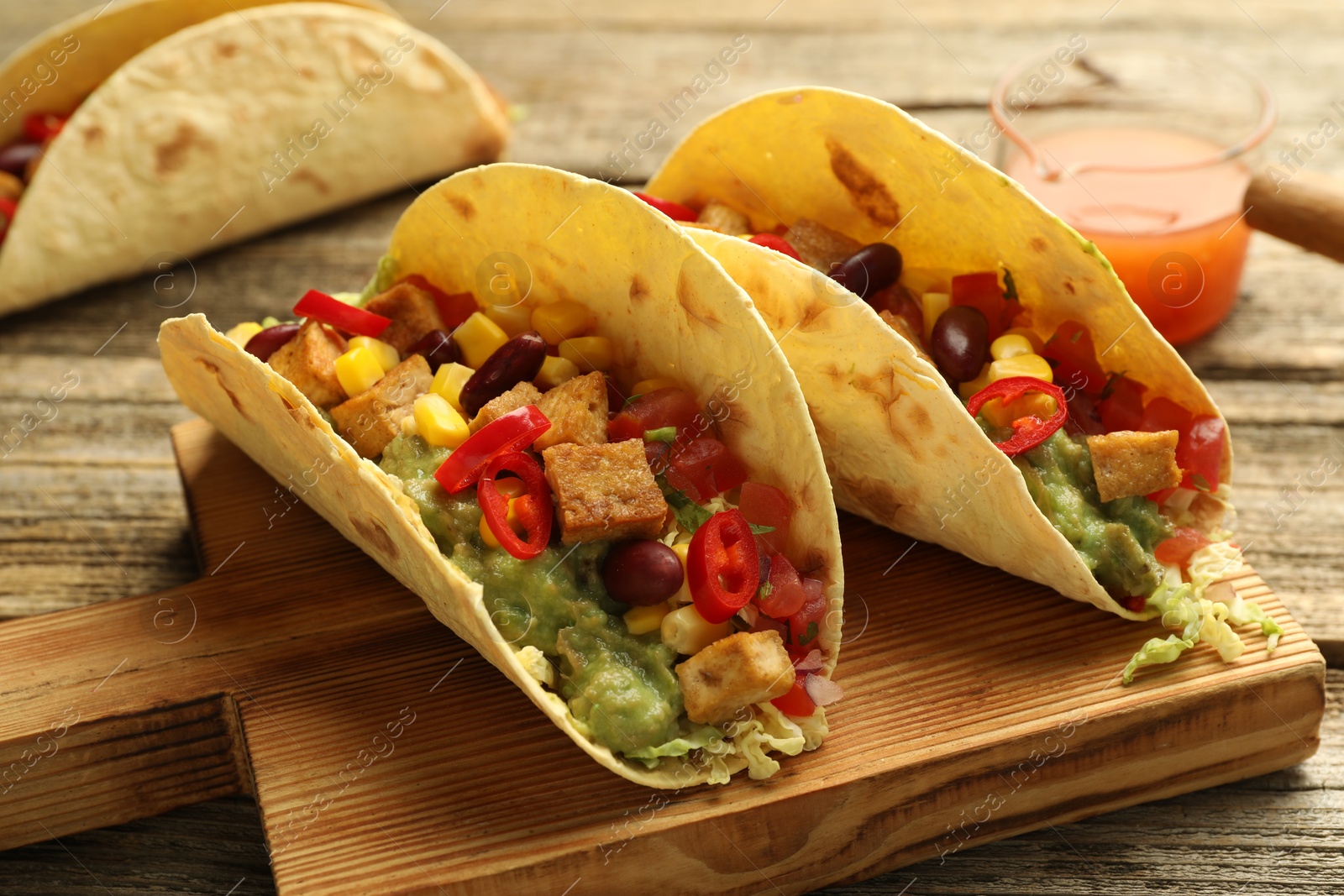 Photo of Tasty vegetarian tacos served with sauce on wooden table, closeup