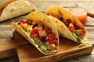 Photo of Tasty vegetarian tacos served with sauce on wooden table, closeup